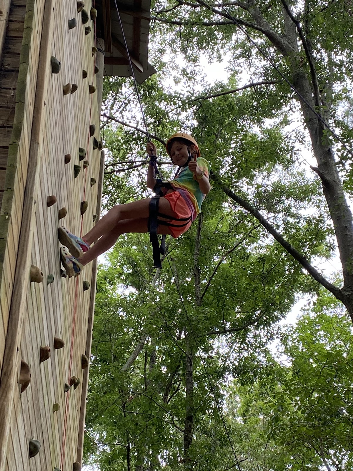 A child repels down a climbing wall while smiling at the camera. 