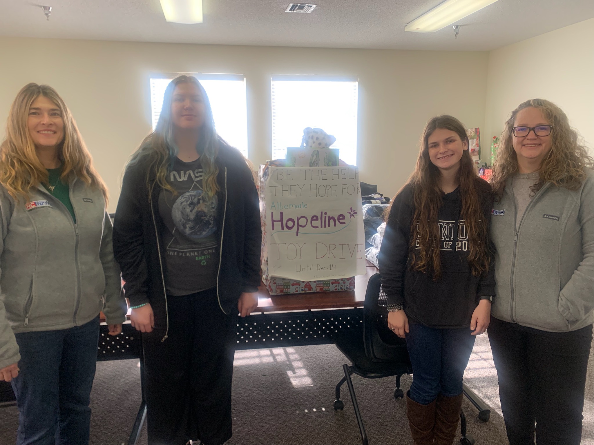 Four women stand beside a toydrive collection box.