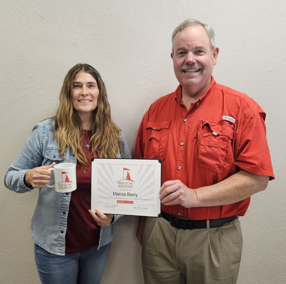 Marcia Berry holds her Wolfpack award and accompanying mug while smiling.