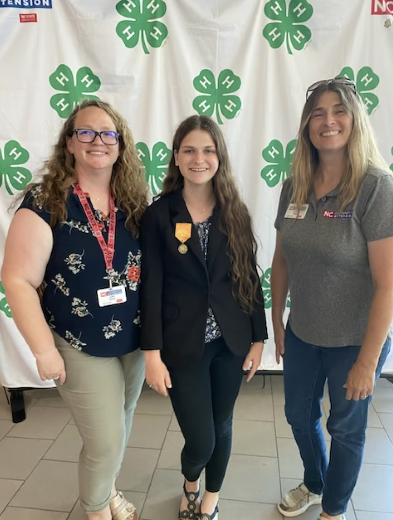 Three women pose in front of a 4-H banner.